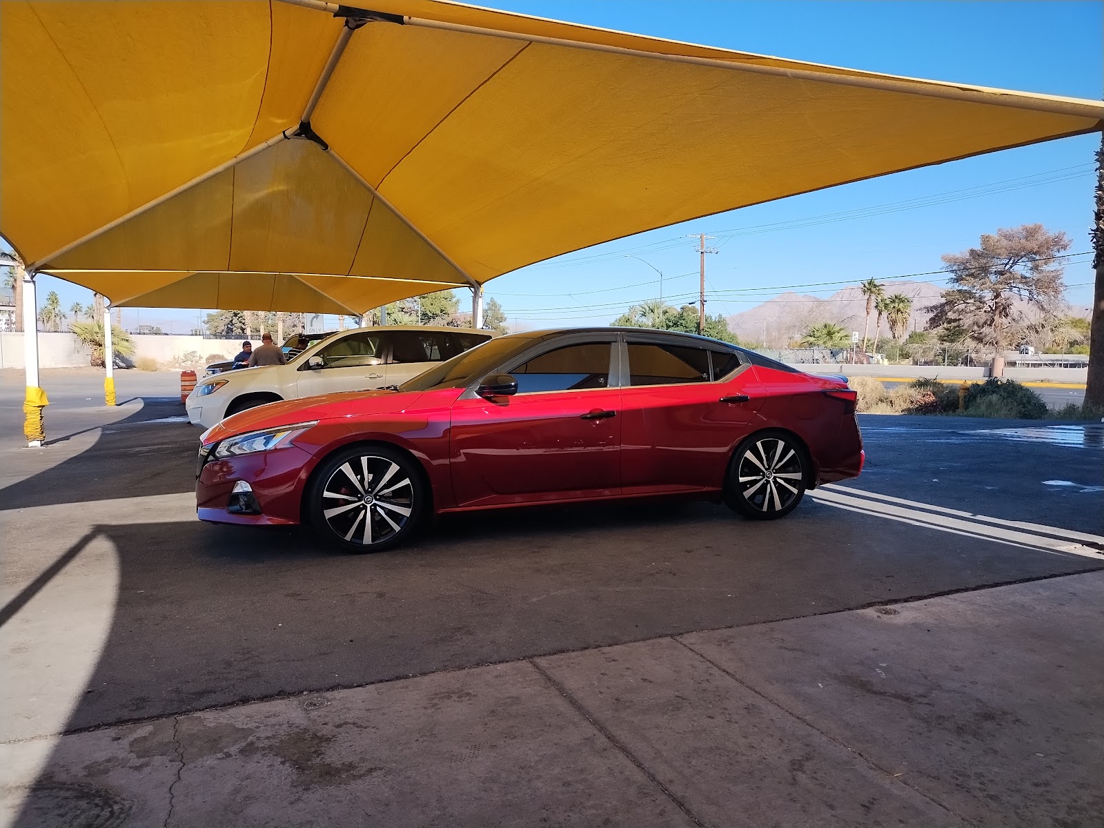 Red Nissan Altima parked under a yellow shade canopy at the car wash